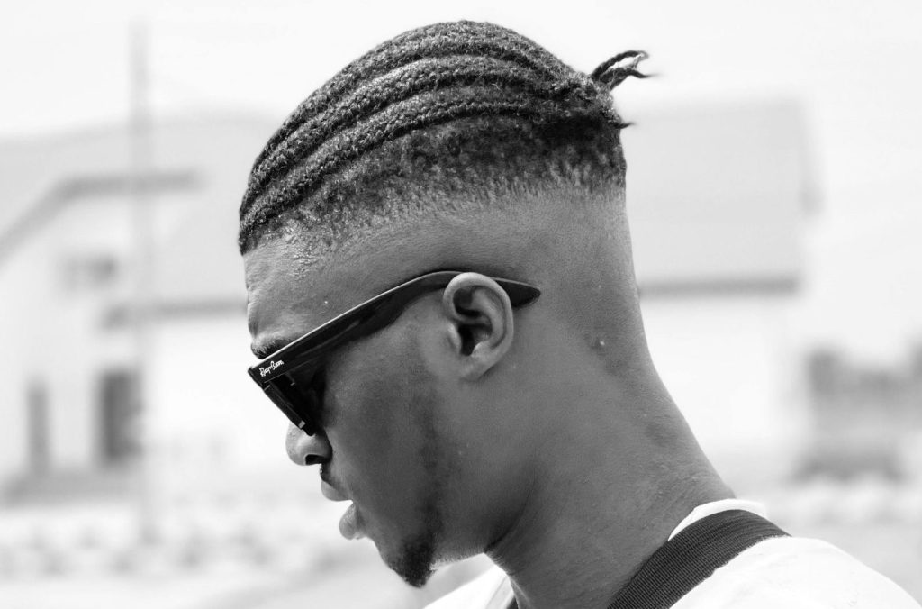 Black and white outdoor portrait of a man with braids and sunglasses in Sagamu, Nigeria.